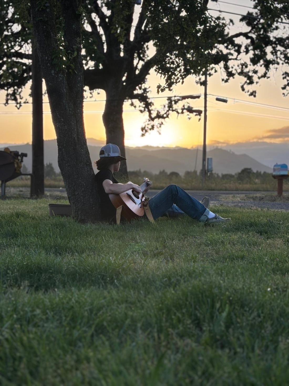 Matteo playing guitar under an oak tree at sunset