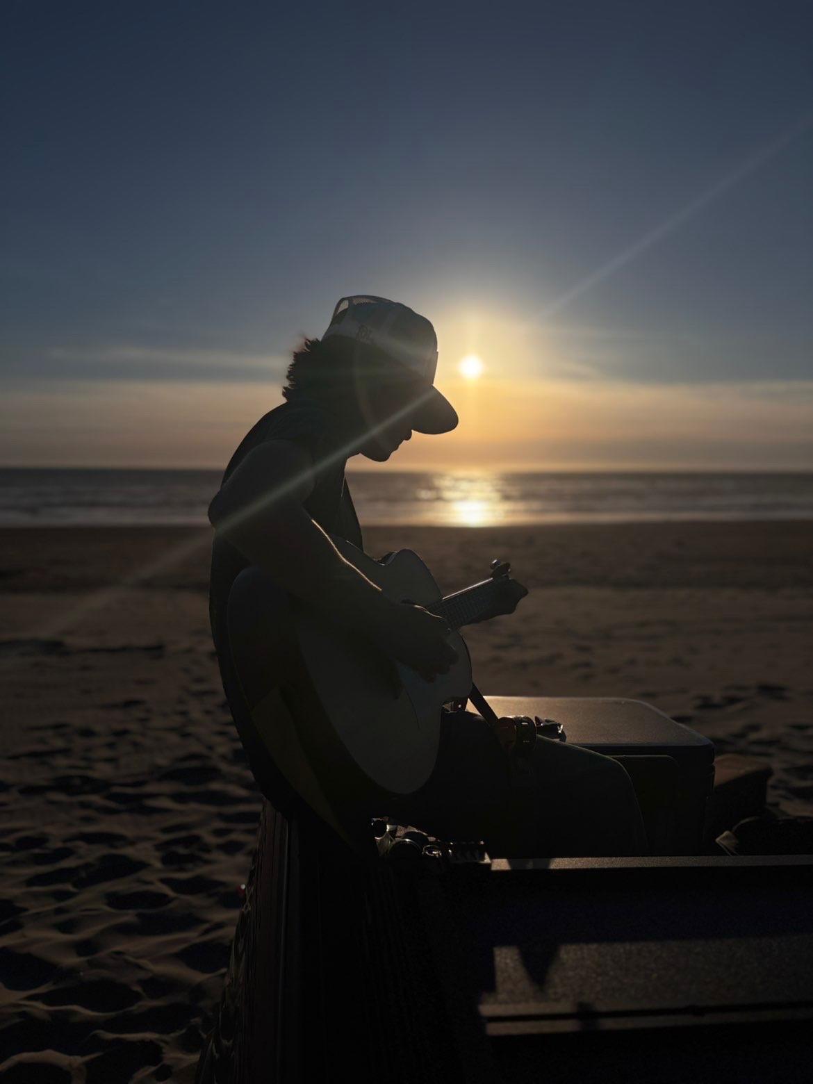 Matteo playing guitar on a tailgate at sunset by the ocean